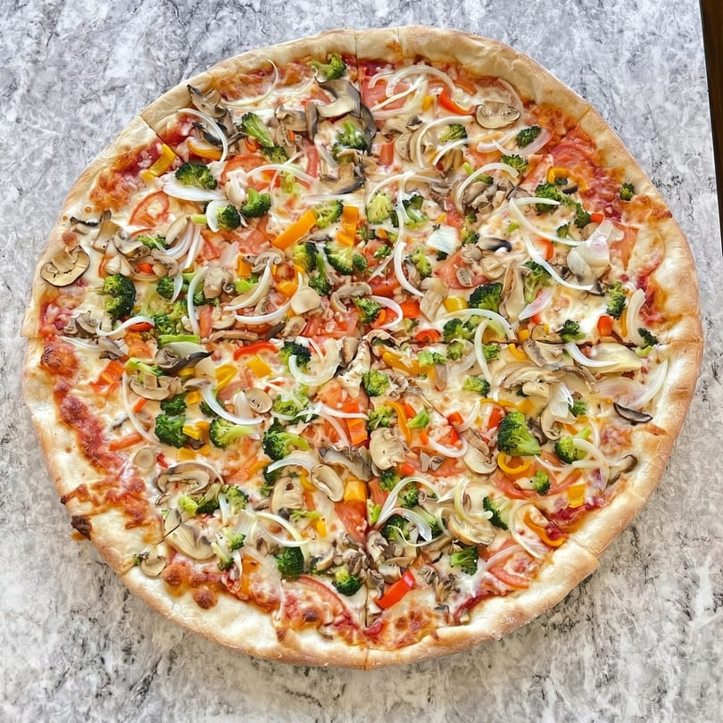 A large, round vegetarian pizza topped with broccoli, mushrooms, onions, and bell peppers.