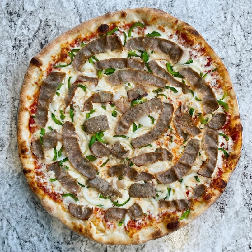 Overhead view of a pizza with sausage, green peppers, and onions on a white marble surface.