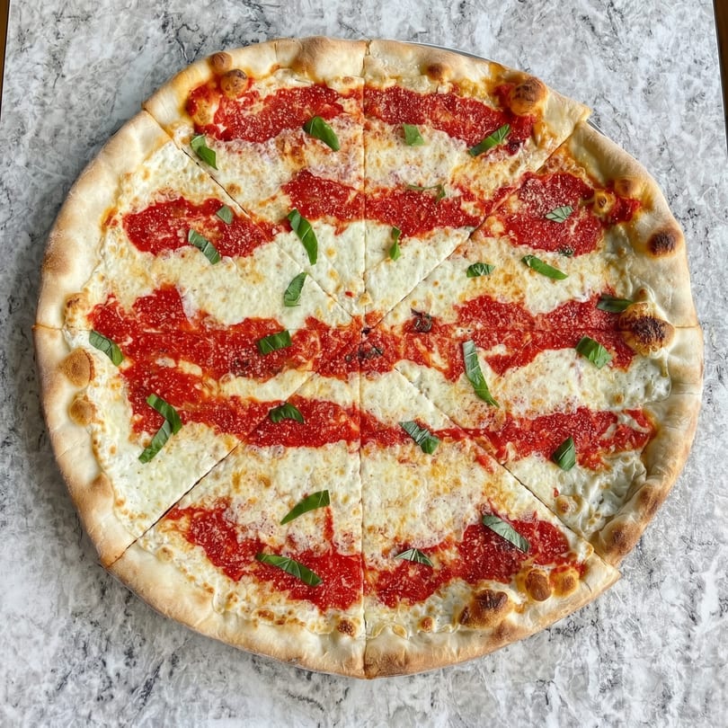 A whole, sliced Margherita pizza with red sauce stripes, mozzarella, and fresh basil on a marble surface.