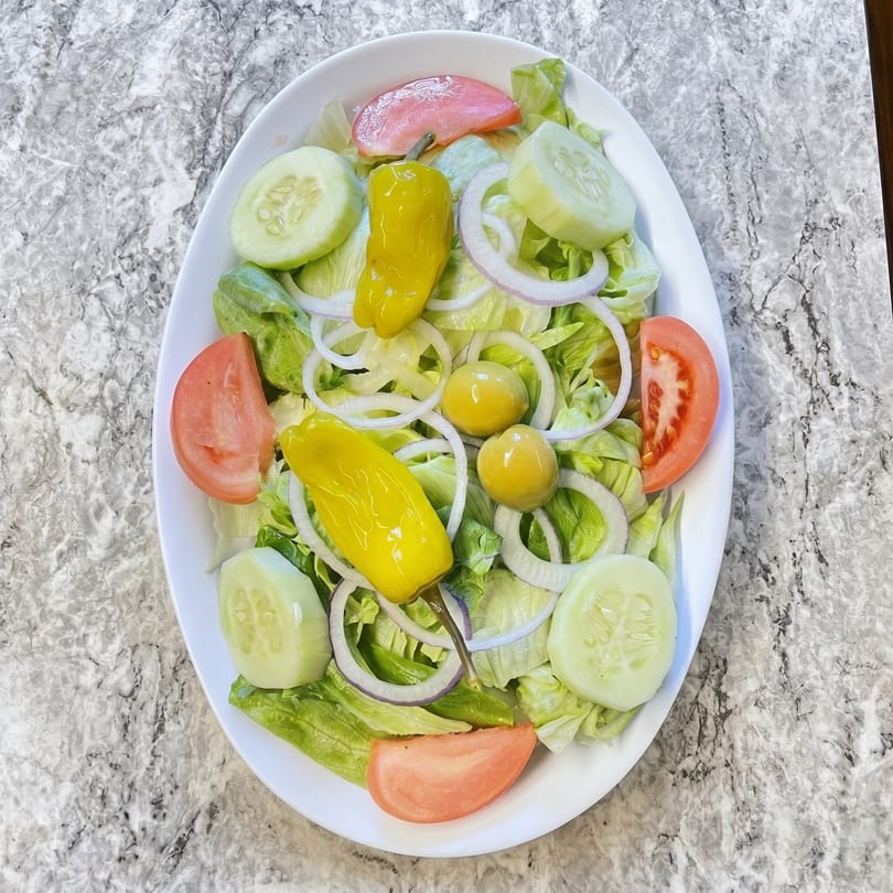 A fresh garden salad with lettuce, tomatoes, cucumbers, onions, pepperoncini, and olives.