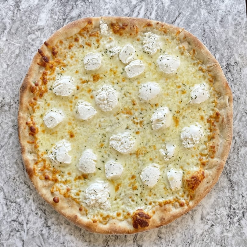 A white pizza with dollops of ricotta cheese and herbs on a marble surface.
