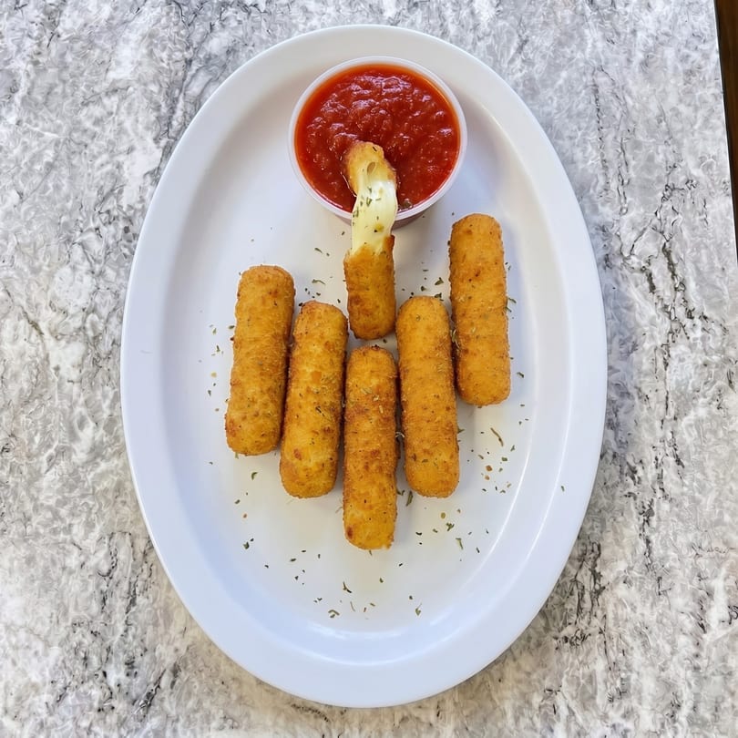 Golden-brown mozzarella sticks with a side of marinara sauce on a white oval plate.